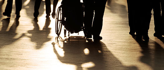 A monotone image of a crowd of people with shadows and silhouettes including a wheelchair